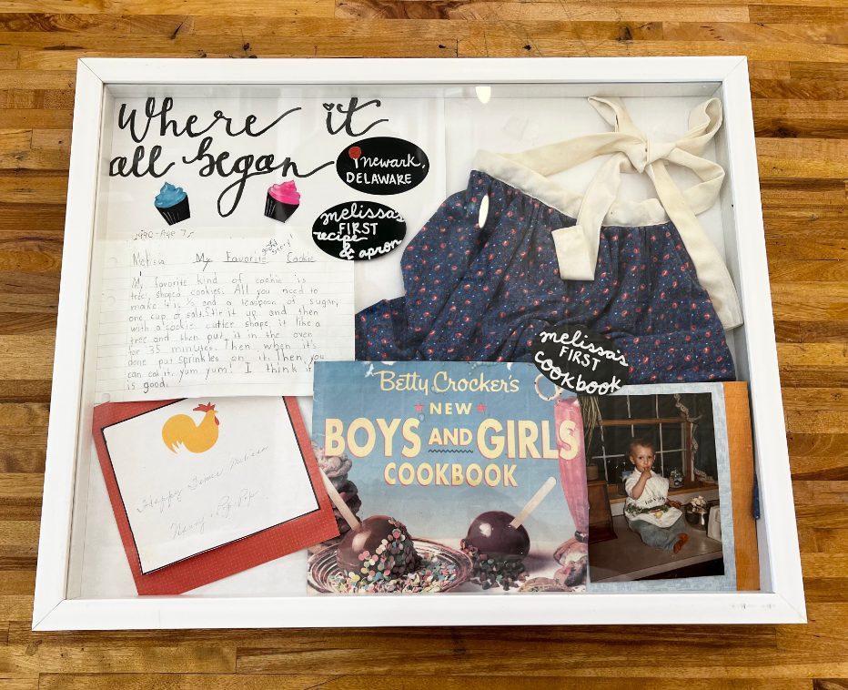 Melissa's Where it all began shadow box with her first recipe, apron, cookbook and a childhood photo