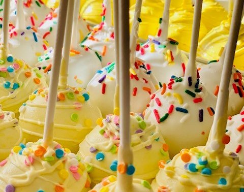 Cake pops dipped in yellow and white with rainbow sprinkles
